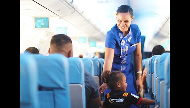 Samoa Airways flight attendant talking with a child on the airplace while another passenger looks on.